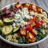 Golden roasted sweet potatoes and bell peppers top a warm quinoa bowl with wilted spinach, finished with a drizzle of vibrant vinaigrette.