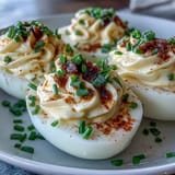Classic deviled eggs with paprika and chives, creamy yolk filling piped into egg whites, garnished with smoky paprika and fresh chives.
