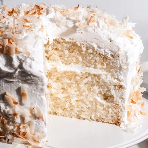 A freshly baked, tender Coconut Cake layered with sweet coconut filling and billowy meringue frosting, ready to slice.