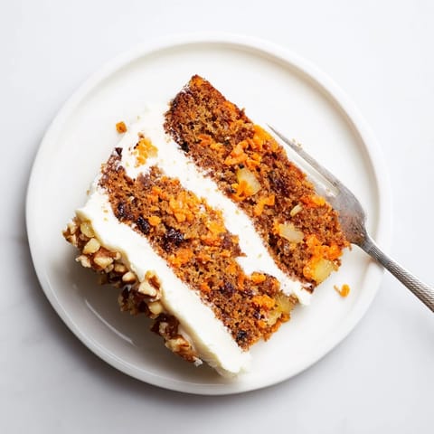 Freshly baked Carrot Cake slice with cream cheese frosting and toasted pecans on a white plate, perfect for dessert.