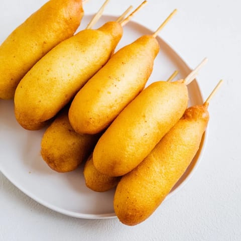 Freshly fried corn dogs on sticks with crunchy coating and soft interior, perfect party snack.