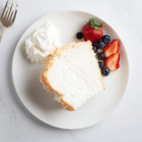 Sliced Angel Food Cake served on a dessert plate with fresh strawberries and a dollop of whipped cream.