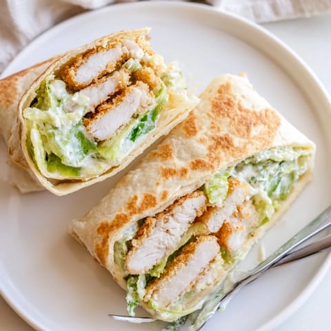 Hearty Crispy Chicken Caesar Wrap sliced in half, revealing layers of crunchy romaine, juicy fried chicken, and melted Parmesan, ready to be enjoyed with a squeeze of lemon.