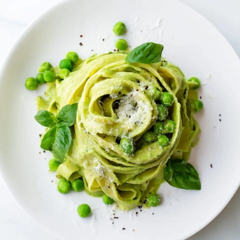 Velvety green pea Alfredo sauce coats fettuccine in a skillet, ready to serve for dinner.  