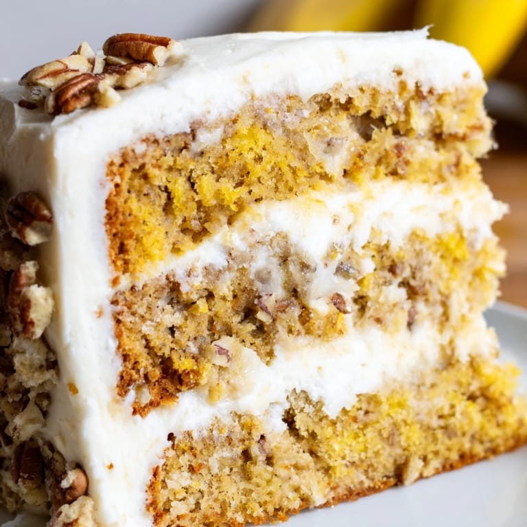 A tall slice of Hummingbird Cake reveals moist crumb, pineapple specks, and swirls of creamy frosting.
