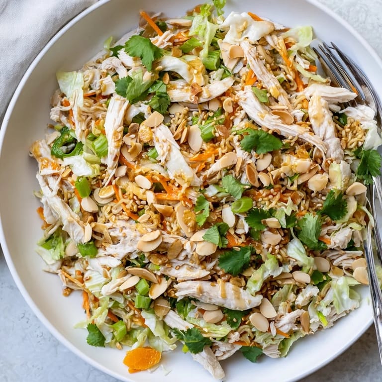 A close-up view of the crunchy ramen chicken salad, with scallions and sesame seeds over a bed of greens.