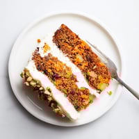 Freshly baked Carrot Cake slice with cream cheese frosting and toasted pecans on a white plate, perfect for dessert.