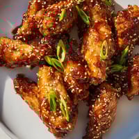 Sticky Asian Sticky Wings resting on a platter, garnished with sesame seeds and green onions for a perfect party appetizer.