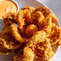 Golden brown, crispy onion petals from Vidalia onions, ready to dip in a bold, spicy sauce.