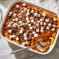 Golden brown Sweet Potato Casserole with toasted marshmallows bubbling in a white dish.