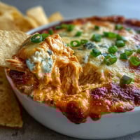 Freshly baked Buffalo Chicken Dip in a white dish, bubbling with melted cheddar and blue cheese.