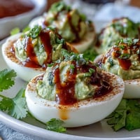 Creamy avocado deviled eggs with a spicy Sriracha drizzle, perfect for healthy party appetizers.  
